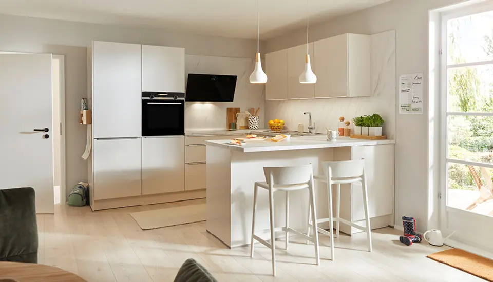 Helle, moderne Küche mit Kochinsel, Hockern und großen Fenstern, durch die Tageslicht fällt.